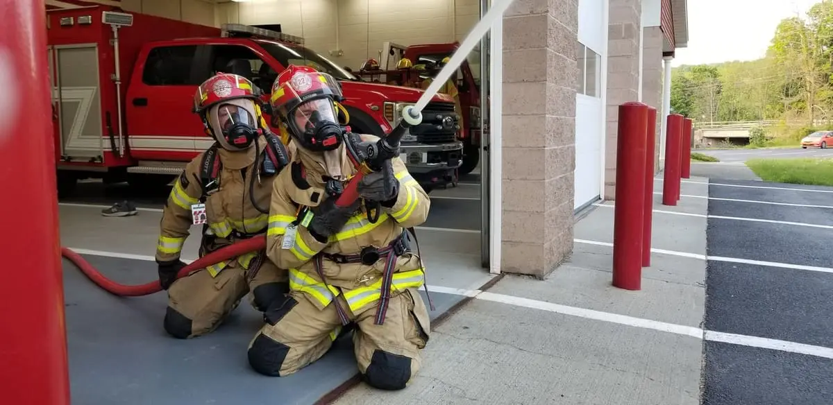 Two Ghent interior firefighters in SCBA air packs and turnout gear advancing a hoseline
